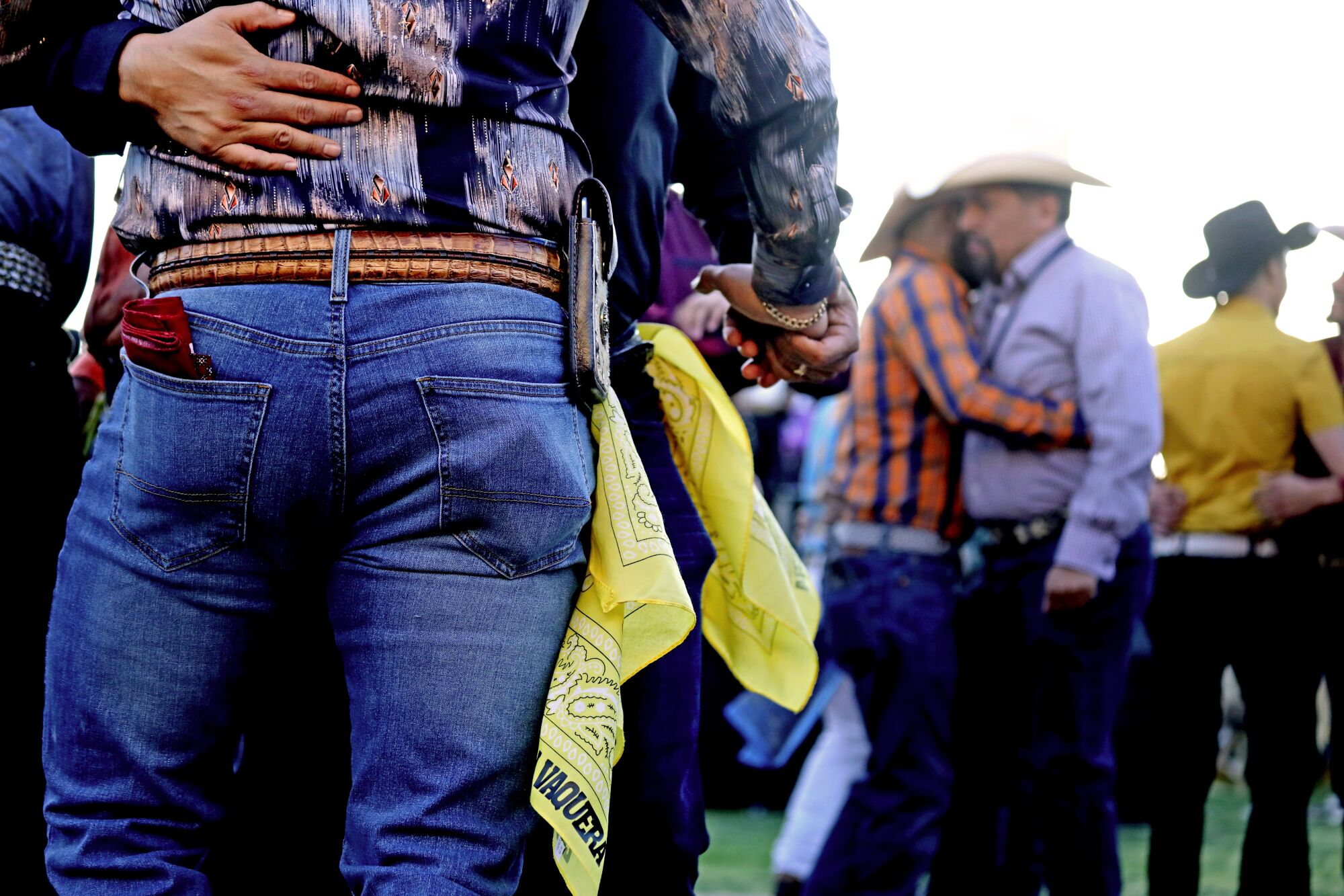 Men in jeans and cowboy hats dance close together during the day at an outdoor venue.