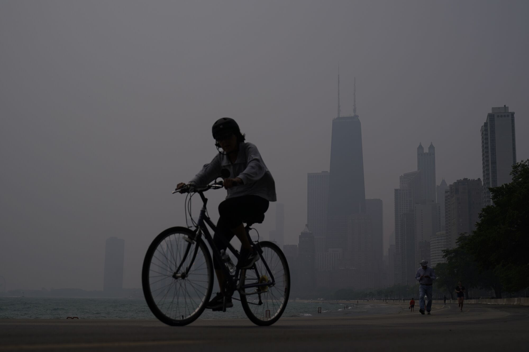 Un ciclista cabalgando en una neblina oscura contra el horizonte de una ciudad parcialmente oscurecida.