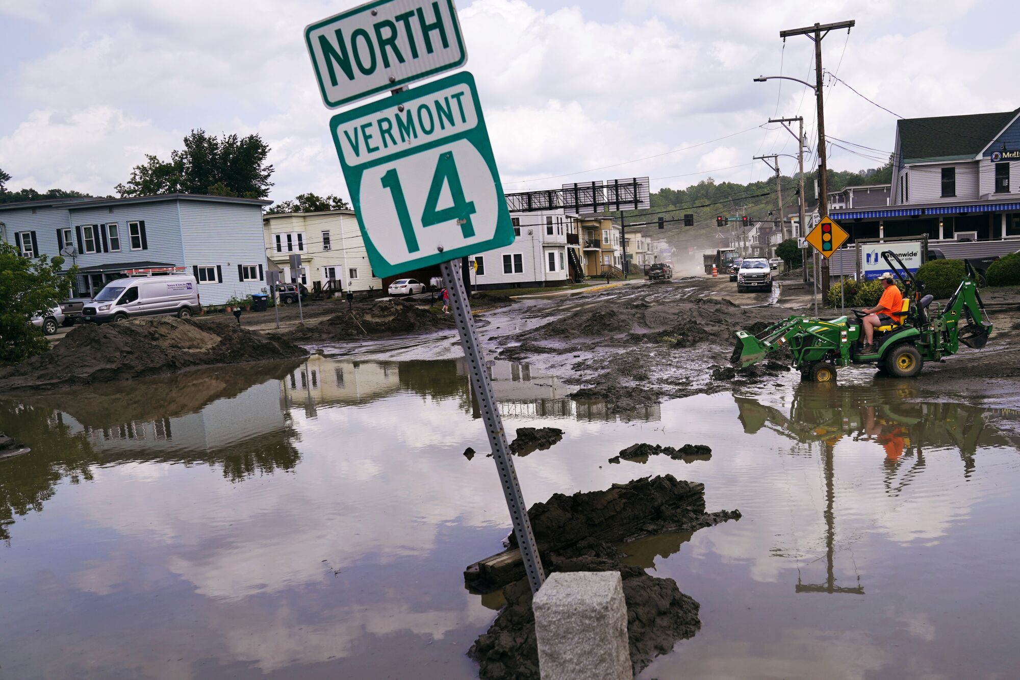 Un pequeño tractor viaja a través del lodo junto a las inundaciones que sumergen parcialmente un letrero que dice "Norte de Vermont 14."